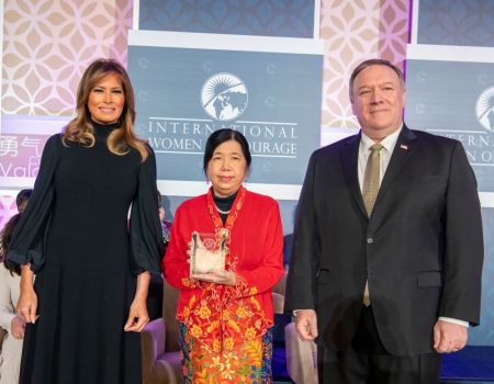 Three people on stage, woman holding award